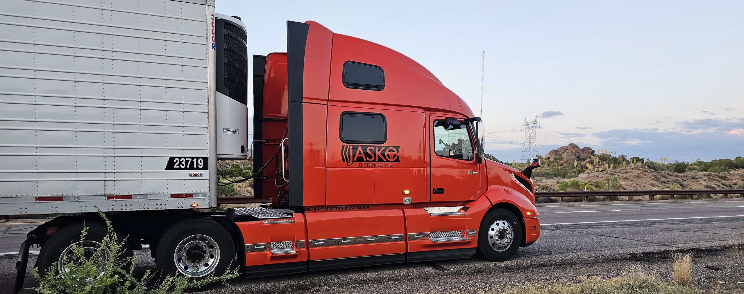 Orange JASKO Volvo tractor and refrigerated trailer on a desert highway at dusk